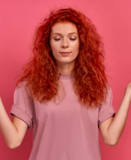 Calm red haired woman relaxing meditation, no stress-free relief at work concept, mindful peaceful young business woman or student practicing breathing yoga exercises, isolated over pink background