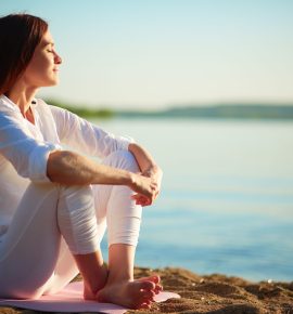 Side view of serene woman sitting on sandy beach against blue sky outdoors