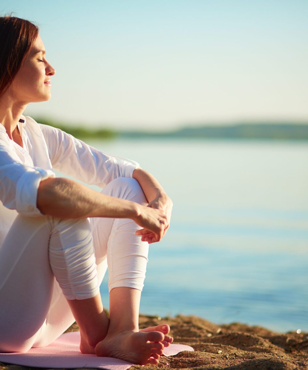 Side view of serene woman sitting on sandy beach against blue sky outdoors